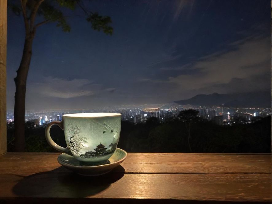 从高处俯瞰广州城市夜景,前景是一个冒着热气的茶杯,营造静谧与繁华的对比