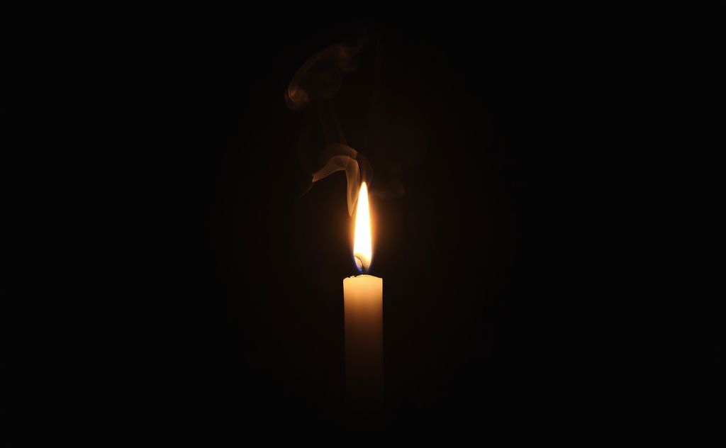 A candle burning in a dimly lit room with smoke rising gently.