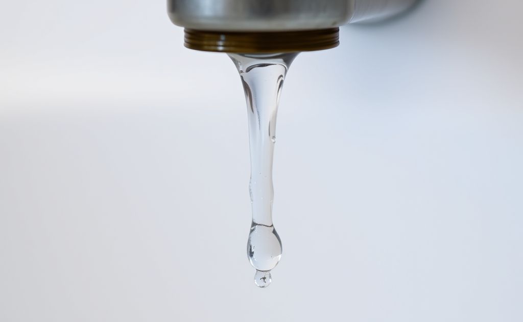 A close-up of a dripping faucet with water pooling below.