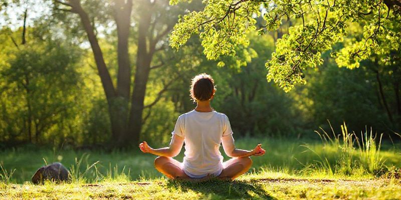A serene person meditating in a peaceful natural setting, bathed in soft sunlight.
