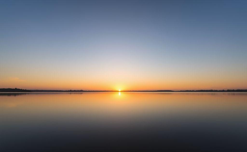 A serene sunrise over a calm lake reflecting clear skies.