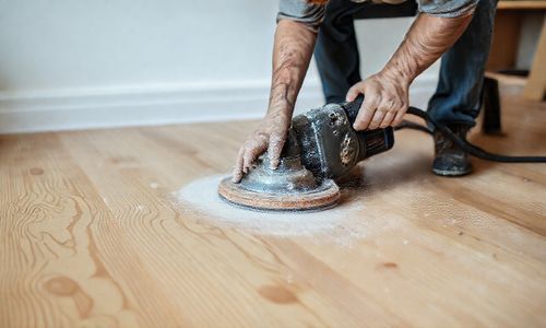 Person sanding a hardwood floor for refinishing